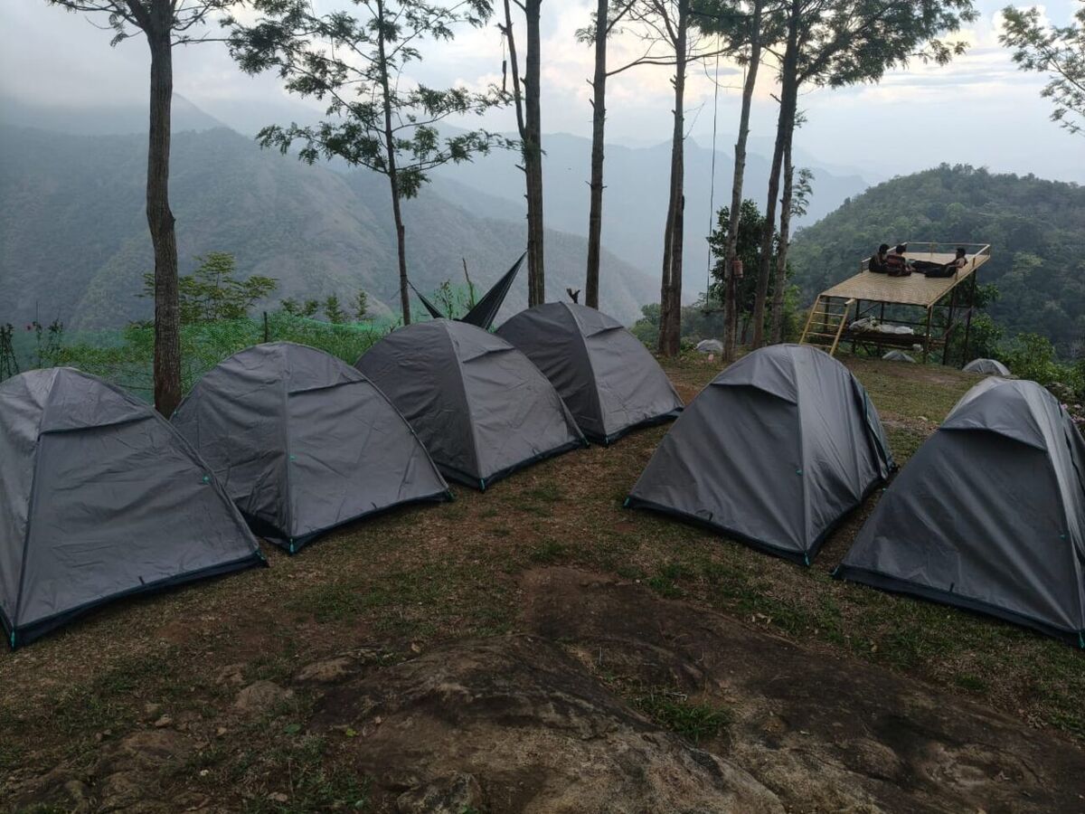 Tents lined along the cliff edge with layered misty ranges behind