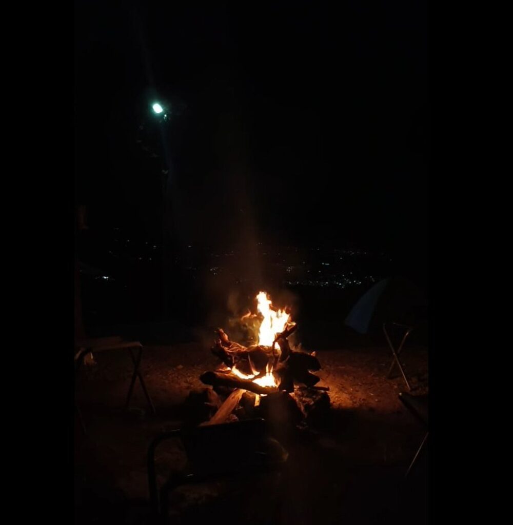 A campfire burning at night above the distant lights of the plains