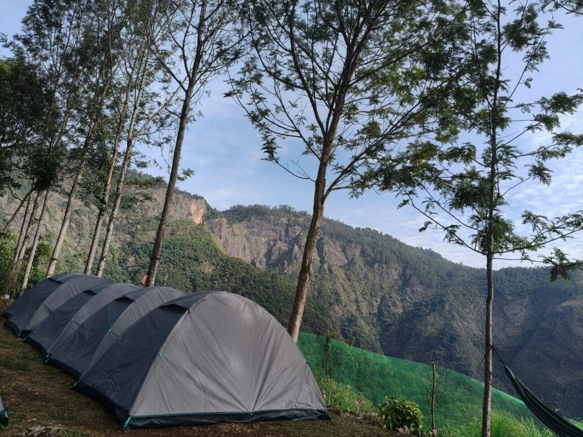 A neat row of camping tents on the grassy spur, mountains beyond